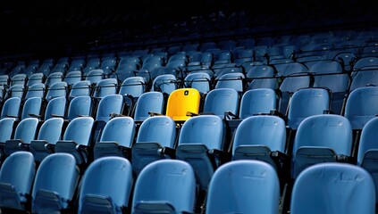 A single yellow seat in a sea of blue stadium chairs