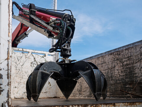 Industrial hydraulic grapple claw attachment inside truck container, showing black jaws, hoses, and rotator. Heavy-duty scrap metal handler used in recycling, salvage, demolition, and construction. - Powered by Adobe