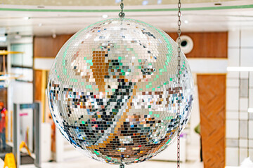 Disco ball suspended from a chain in a blurred, upscale interior with wood paneling Reflective mirrors create colorful patterns suggestive of ambient lighting