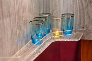 A minimalist image showcases a row of blue glasses arranged on a white shelf against a textured...