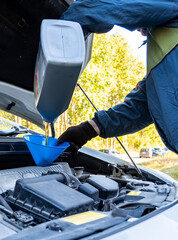 A man pours motor oil from a plastic canister into a car engine. Car servicing outdoors.