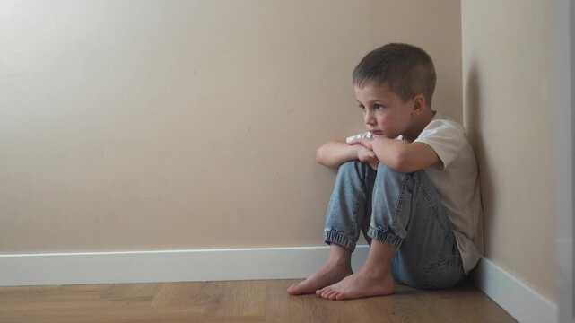 Young girl sitting on the floor. Sad child sits on a corner and is punished. A teenage girl lifestyle is traumatized by a violent incident. A little girl sitting on the ground.