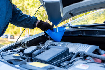 A man pours motor oil from a plastic canister into a car engine. Car servicing outdoors.