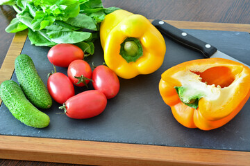 bell peppers, plum tomatoes, cucumber and greens on the cutting board
