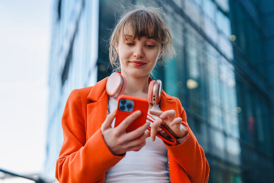 A smiling woman is using her mobile phone while standing near a modern building in Midtown