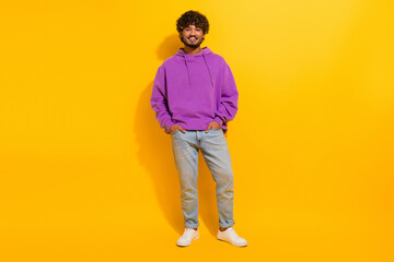 Fototapeta premium Young man wearing a vibrant purple hoodie, posing with a confident smile against a bright yellow background.