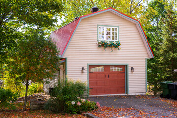 Pretty pink two-story clapboard barn with red door and gambrel metal roof seen in the fall in a rural village, Neuville, Quebec, Canada © Anne Richard