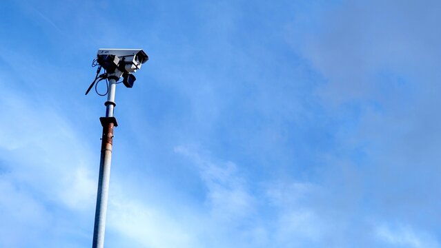 A modern CCTV security camera on a tall pole against a bright blue sky, a concept of public safety and monitoring