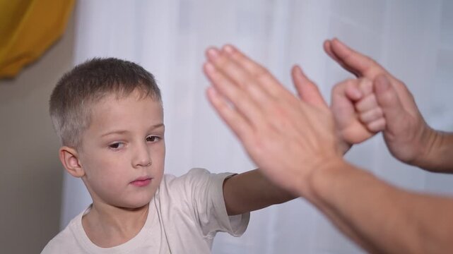 Boy learns punching from coach during martial training session. Coach demonstrates technique, boy repeats punch focus. Martial rhythm helps boy master coach instructions while improving coordination.