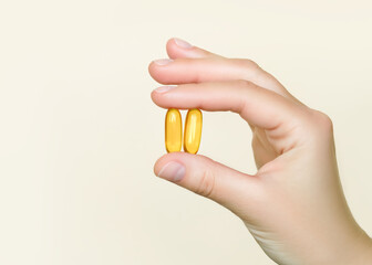 Hand holding two yellow vitamin capsules