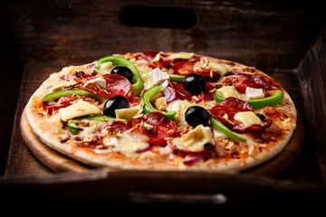 Pizza with chorizo ​​sausage, mozzarella cheese, green pepper and black olives. Rustic wooden background. Soft focus.	
