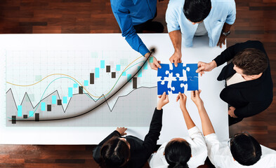 A diverse team collaborates on financial strategy by analyzing graphs and fitting puzzle pieces together, symbolizing teamwork in a modern office setting. Axiom