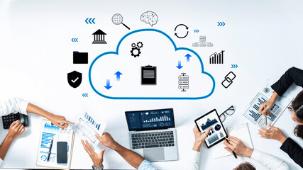 Professionals collaborate around a table using digital devices, discussing cloud technology while analyzing data through charts and graphs in a modern workspace. Trope
