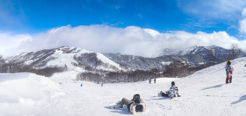 Snowboarders taking a break and enjoying the panoramic mountain view on a sunny day (Maiko, Minamiuonuma, Niigata, Japan)