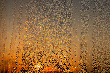 Obraz premium water droplets from condensation on the window glass at sunset, wet glass with lots of water droplets on the background of an orange sky