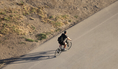 Aerial top top view of man sporty male Cyclist with rucksack backpack wearing black shorts and shirt riding a bicycle on asphalt road background Sportsman Sunset light. Evening time. Golden hour
