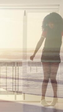 Animation of sunset beach over teenage girl dancing at home