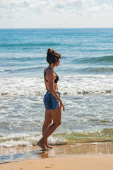 A woman is standing on the beach wearing a black bikini and listening to music