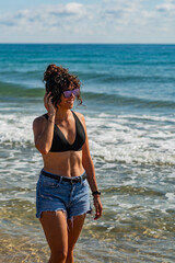 A woman is standing on the beach wearing a black bikini and listening to music