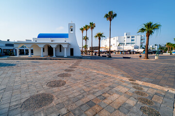 White Greek-style church with palm-trees on square in port Ayia Napa, Cyprus. Mediterranean landscape in tourist town.