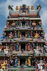 Naklejka premium Detailed view of a colorful Hindu temple gopuram (tower) adorned with intricately sculpted deities, mythological figures, and ornate patterns. The vibrant statues in multiple tiers represent Hindu