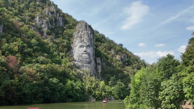 Danube river flowing through the Iron Gates gorge in Romania, featuring the ancient Dacian King Decebalus sculpture carved into the mountain, with small boats cruising on the water