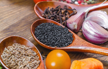 Black sesame seeds, cloves and cumin in wooden spoons. Garlic and cherry tomatoes. Wooden background