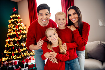 Family celebration in cozy home with festive Christmas tree, wearing matching red sweaters and...