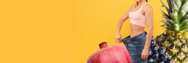 Cheerful young woman demonstrates her weight loss journey by proudly holding out the waistband of...