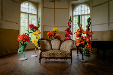 An old, ornate sofa sits in a vintage room with large, colorful artificial flowers, a mix of elegance and fantasy.