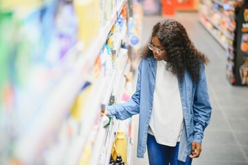 A african american young woman chooses household chemicals in a supermarket. Means for washing and...