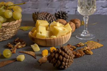 Grape clusters with cheese and walnuts on a wooden board, decorated with dry leaves and pinecones in a cozy autumn scene