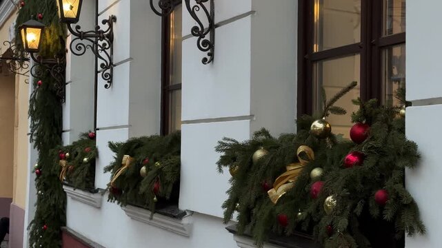 Festive street decorations featuring lush evergreen garlands adorned with red and gold ornaments, creating a warm holiday atmosphere on a charming building facade