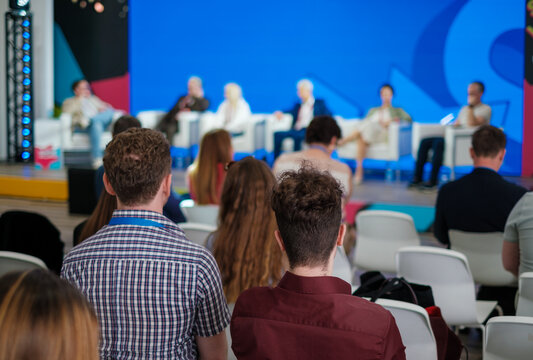 Panel discussion stage with diverse speakers and attentive audience at conference colorful backdrop - Powered by Adobe