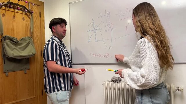 Teen students solving math problems and discussing graph equations on a whiteboard during a collaborative study session indoors