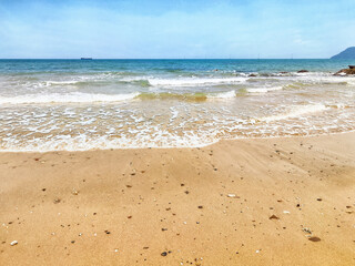 Waves gently lap against the shore on a sunny day at a tranquil beach in a coastal area