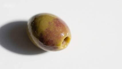 A single green and purple olive with a pitted end, resting on a white surface.