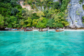 Four traditional thai longtail boats are resting in the calm turquoise water of Monkey Bay. With lush vegetation and limestone cliffs in the background. Located in Phi Phi Don Island. Krabi. Thailand