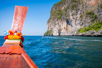 Longtail boat navigating tropical turquoise sea near a towering limestone cliff on Ko Phi Phi Don, offering a unique perspective of this iconic Thai island destination