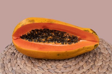 Half of a papaya with juicy orange pulp and seeds exposed, lying on a straw mat. Exotic tropical fruit closeup symbolizing healthy diet, freshness, natural vitamins, and organic food lifestyle.