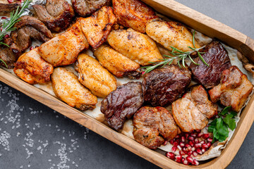 Grilled meat assortment close-up. Close-up view of grilled chicken wings, beef, and pork served with herbs and pomegranate seeds.