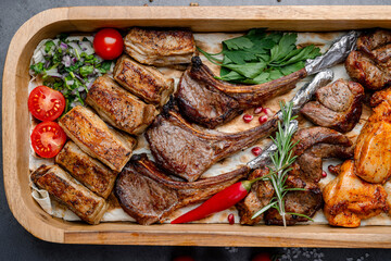 Grilled lamb ribs close-up. Close-up of roasted lamb ribs served on a wooden tray with herbs, chili, tomatoes and pomegranate.