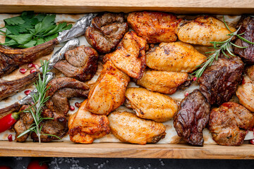 Roasted meat platter. Grilled lamb chops, chicken wings, and beef served on a festive wooden tray with herbs and tomatoes.