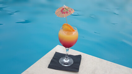 Colorful Summer Cocktail with Orange Slice and Umbrella by Swimming Pool