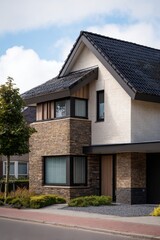 A contemporary two-story residence featuring elegant stone and wooden accents is situated in a charming suburban neighborhood, basking in the sunshine