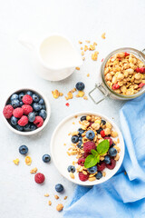 Yogurt with fresh berries and granola on white table.