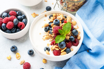 Yogurt with fresh berries and granola on white table.