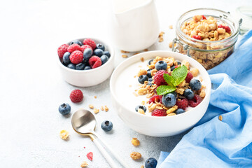Yogurt with fresh berries and granola on white table.