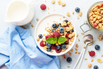 Yogurt with fresh berries and granola on white table.