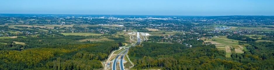 Fototapeta premium Path of Progress: Expansive Aerial Panorama of a New Highway Carving Through a Vast Forest Landscape
